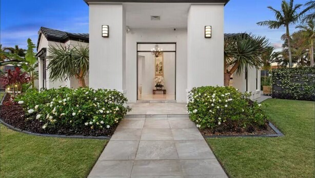 A modern house with a central entrance, surrounded by well-maintained gardens and palm trees. - Spacious 4BR Poolside Escape (Burleigh Waters)