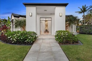 A modern house with a central entrance, surrounded by well-maintained gardens and palm trees. - Spacious 4BR Poolside Escape (Burleigh Waters)