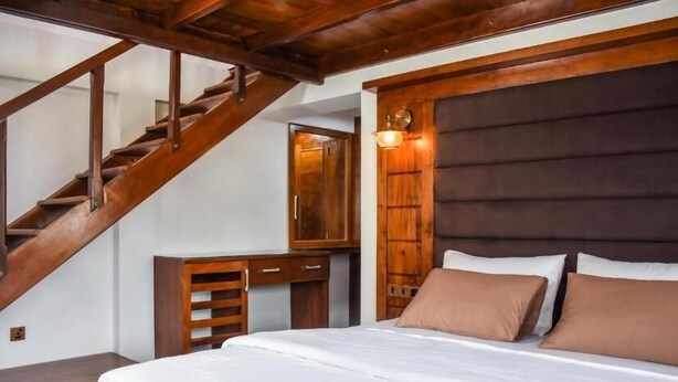 Une chambre avec un escalier en bois, un lit avec une literie blanche et une tête de lit en bois.