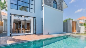 Ein modernes Haus mit Pool, einem Essbereich mit Gartenmöbeln und einem großen Fenster mit Blick auf den Pool.