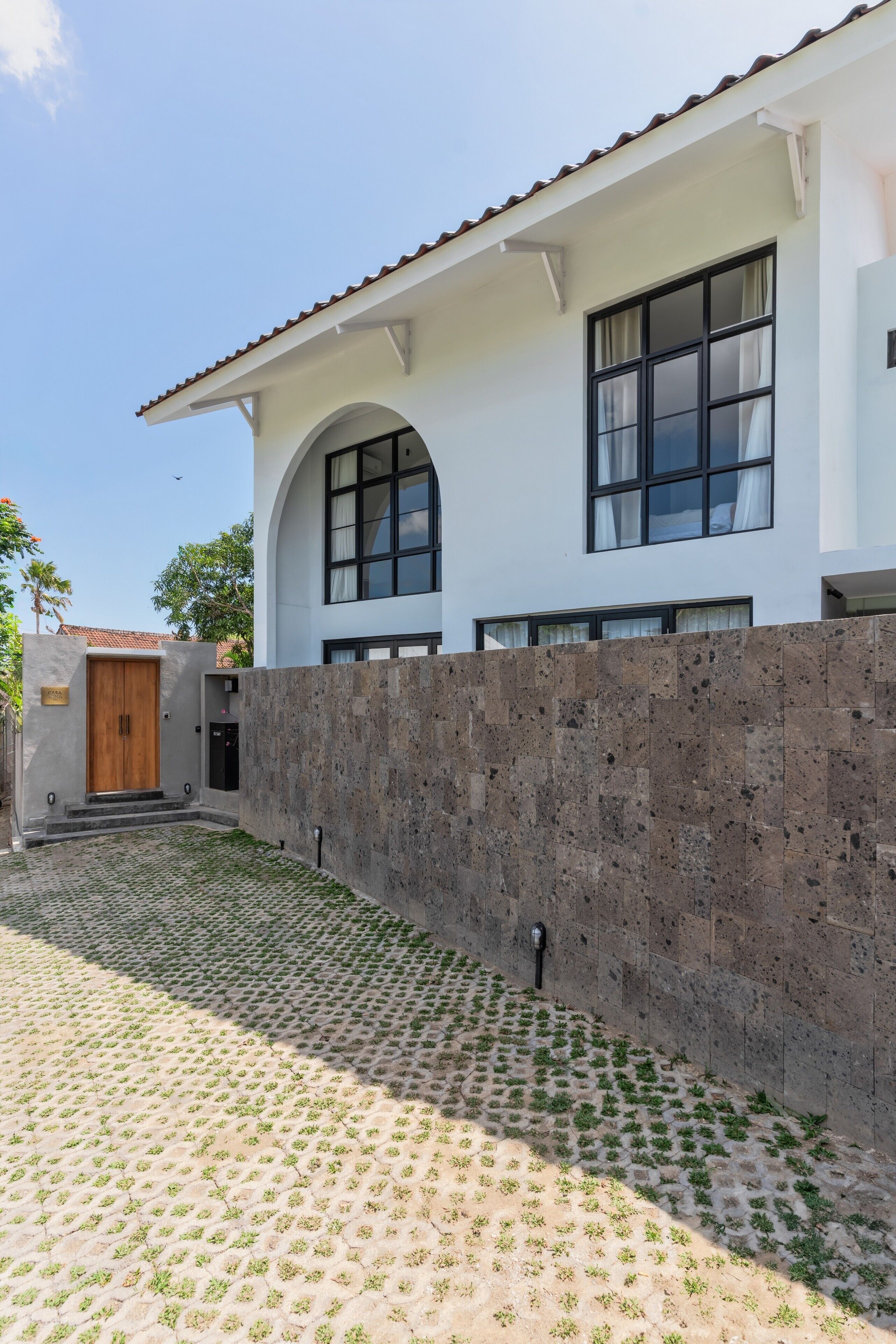A modern house with a stone wall, a wooden door, and a tiled courtyard.
