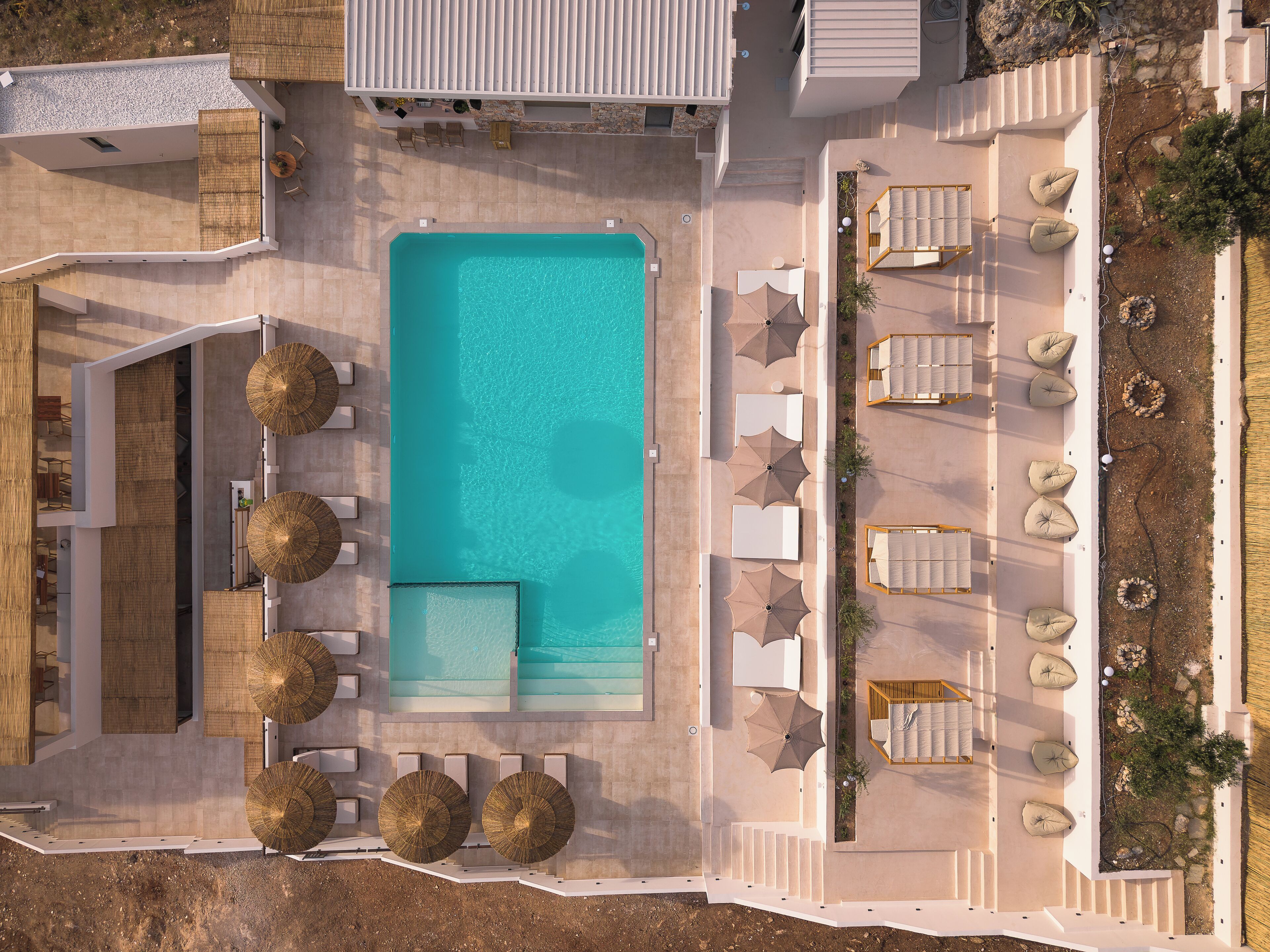 An aerial view of a resort with a central swimming pool, sun loungers, and a seating area with umbrellas.
