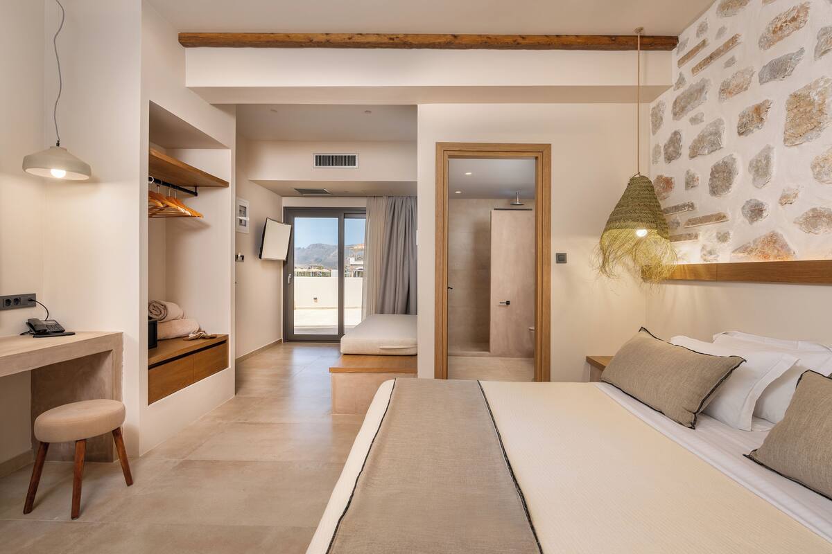 Un dormitorio moderno con cama, escritorio y silla. Se aprecia vista al exterior a través de un ventanal.