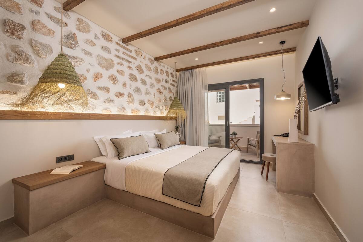 Un dormitorio con cama, mesitas de noche, televisor y pared con diseño de piedra.