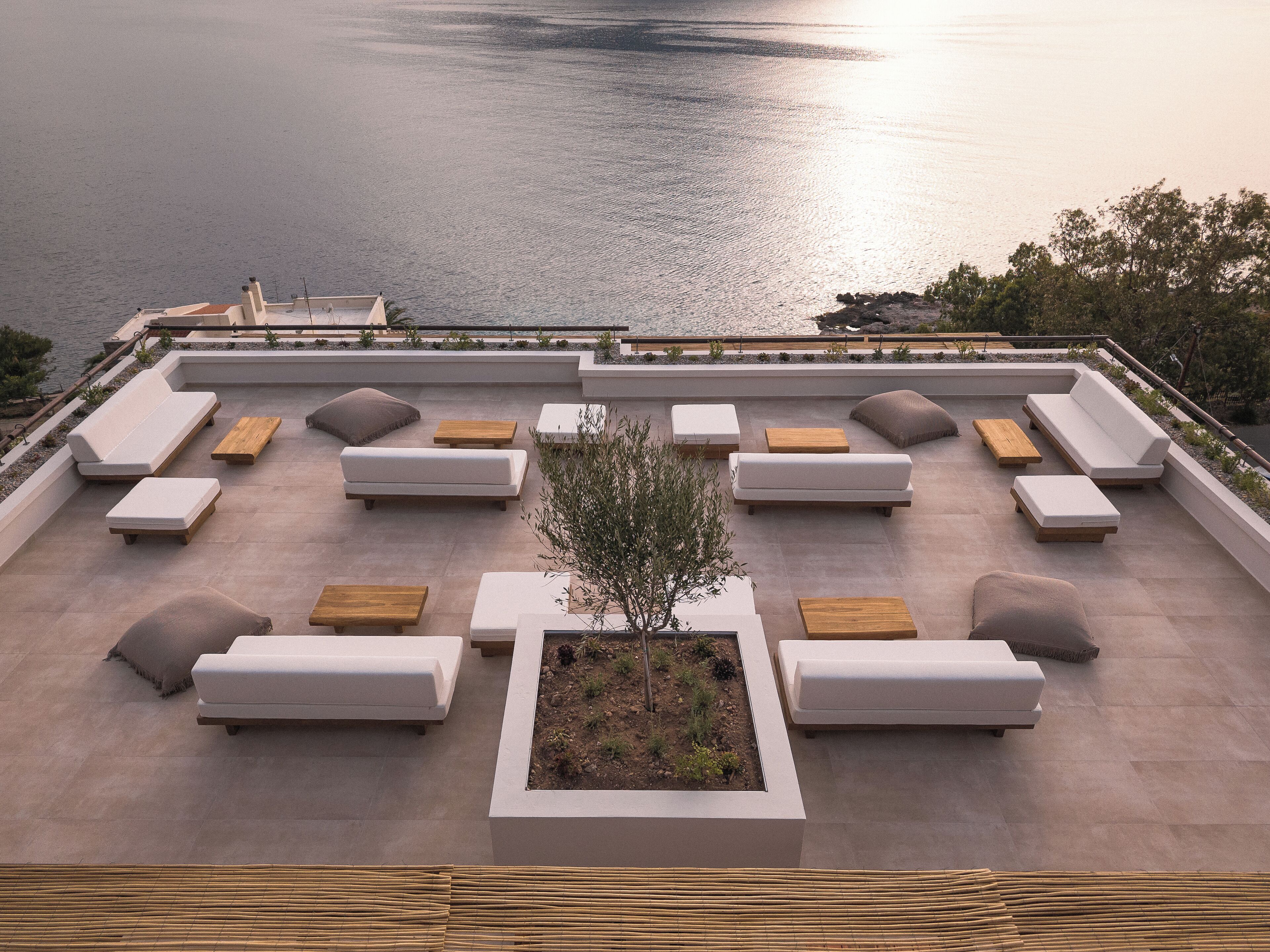 Eine Dachterrasse mit verschiedenen Sitzbereichen, einem kleinen Baum und Blick auf das Wasser.
