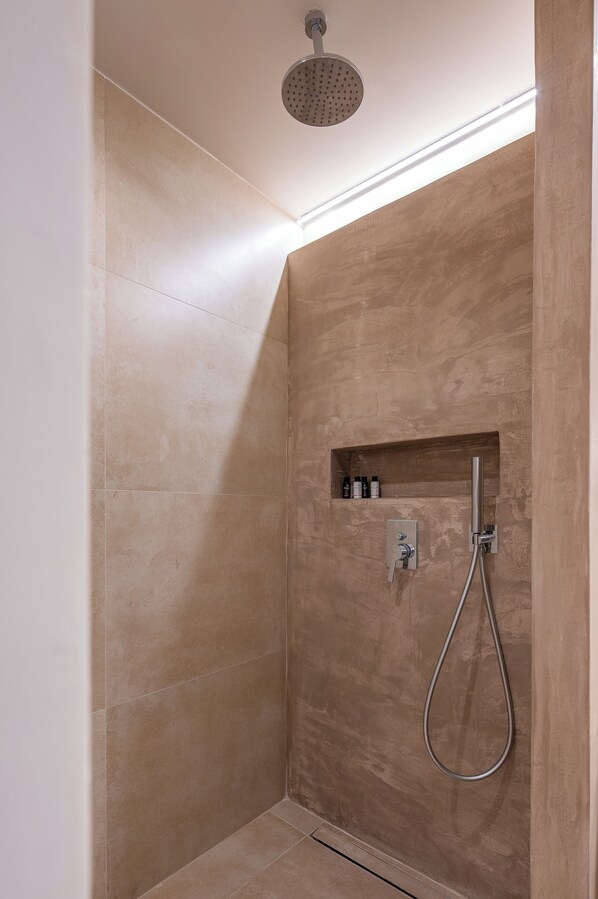 Un espace douche moderne doté d’un pommeau de douche à main, d’une étagère intégrée pour les articles de toilette et d’un panneau de commande fixé au mur.