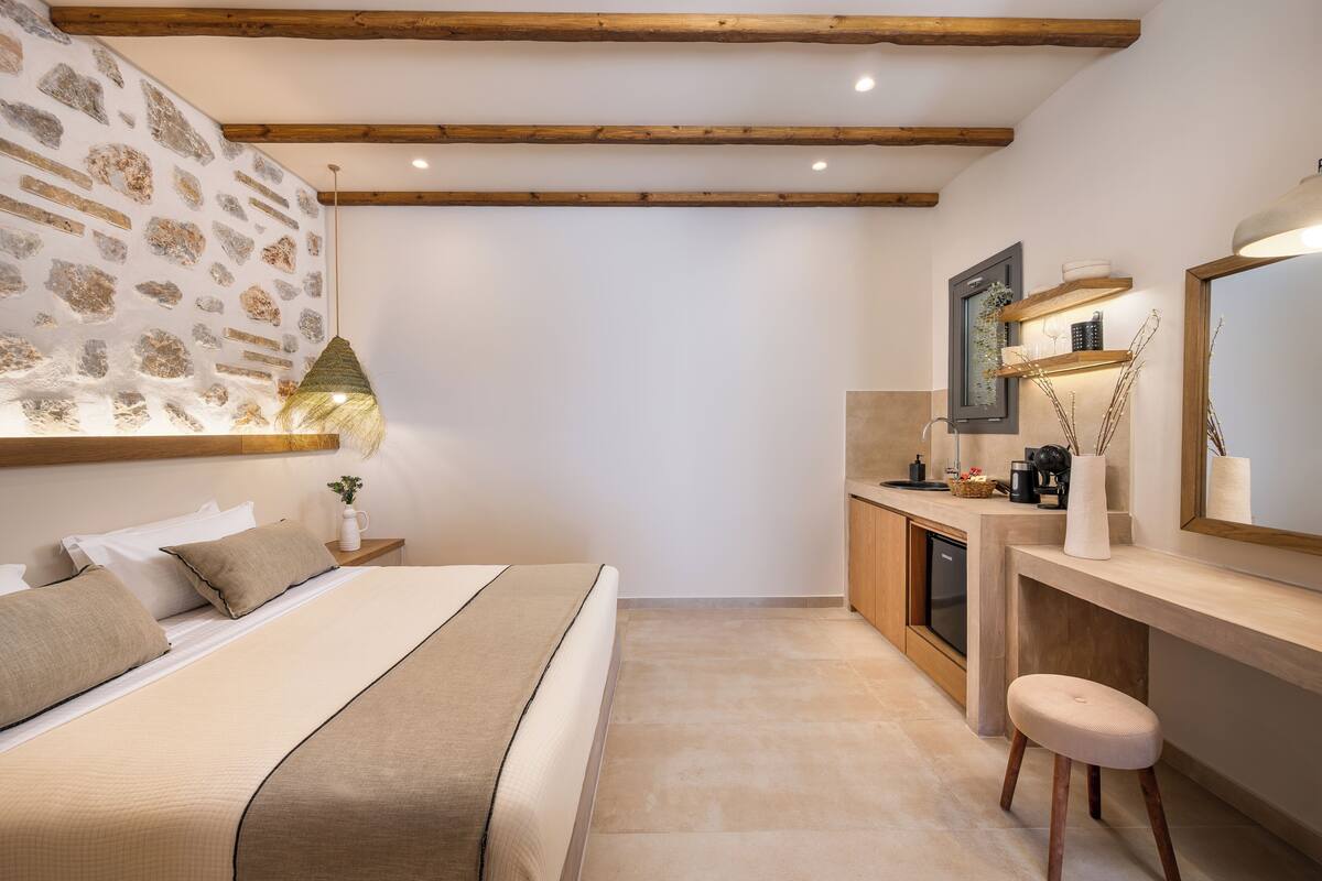 Un dormitorio con cama, mesita de noche, lámpara y un taburete pequeño.