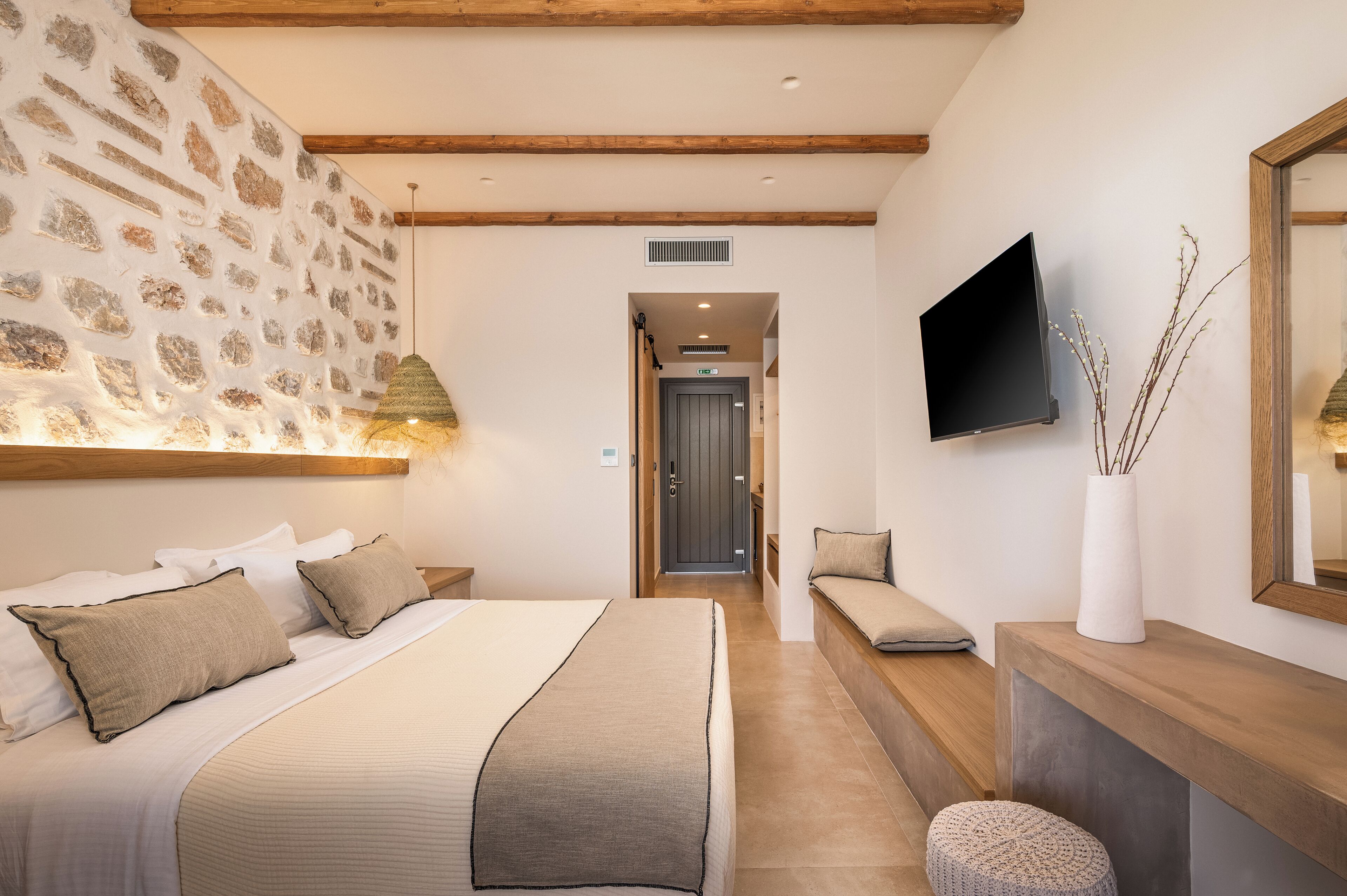 A hotel room with a bed, bedside tables, a TV, a bench, and a wall-mounted TV.