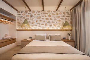 Un dormitorio con pared de piedra, vigas de madera, una cama con almohadas, una mesita de noche, una lámpara colgante y una ventana con cortinas.