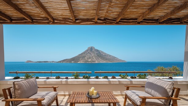 Eine Terrasse mit Holzmöbeln, einem Tisch mit Kerzen und Blick auf das Meer und ein Berg.