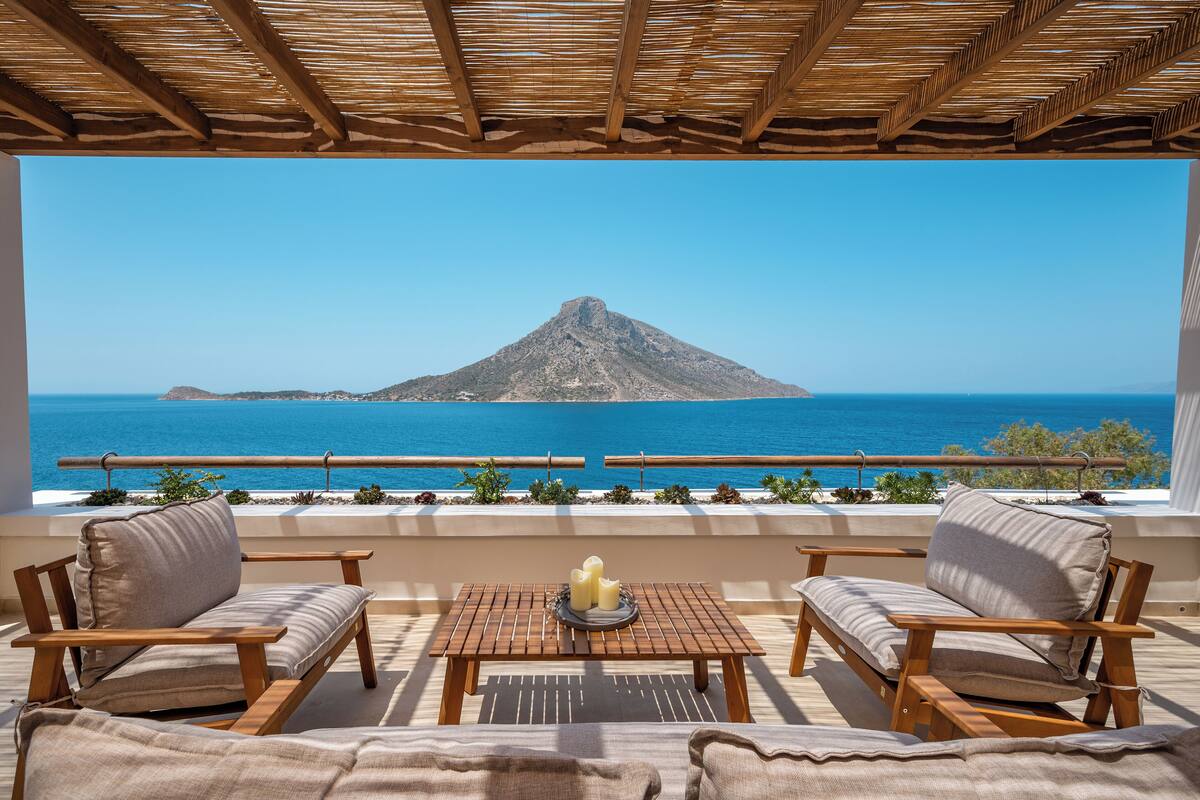 Una terraza con mobiliario de madera, una mesa con velas y vistas al mar y a una montaña.