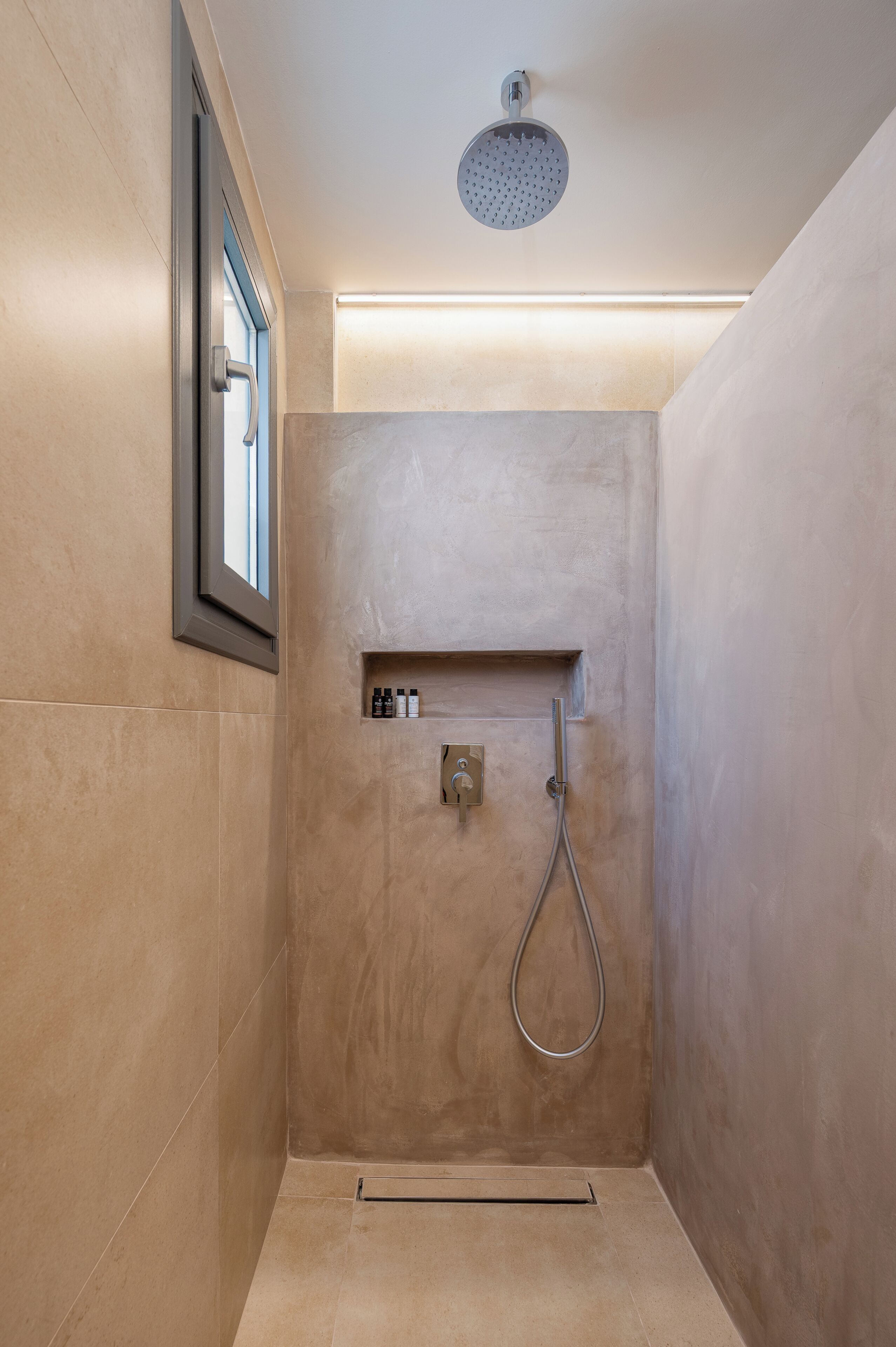 A shower with a handheld showerhead, a small shelf with toiletries, and a window with a view.