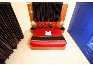 A bed with a red and black bedspread, two nightstands with lamps, a blue wardrobe, and a curtain. - Dreams Neelankarai (Chennai)