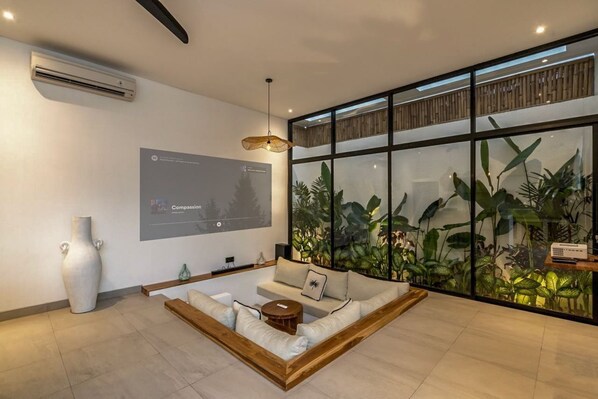 A modern living room with a large window, a sofa, a coffee table, and a projector screen displaying a presentation titled "Compassion."