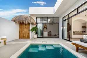 A modern poolside area with a thatched-roof structure, a lounge chair, and a pool.