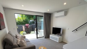 A modern living room with a grey sofa, a brown leather chair, a small wooden table, and a TV on a white stand. - New Merivale townhouse, centrally located by Hagley Park and City. (Christchurch)