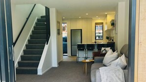 A modern interior with a staircase, a living area with a sofa and a coffee table, and a kitchen area with a refrigerator and cabinets. - New Merivale townhouse, centrally located by Hagley Park and City. (Christchurch)