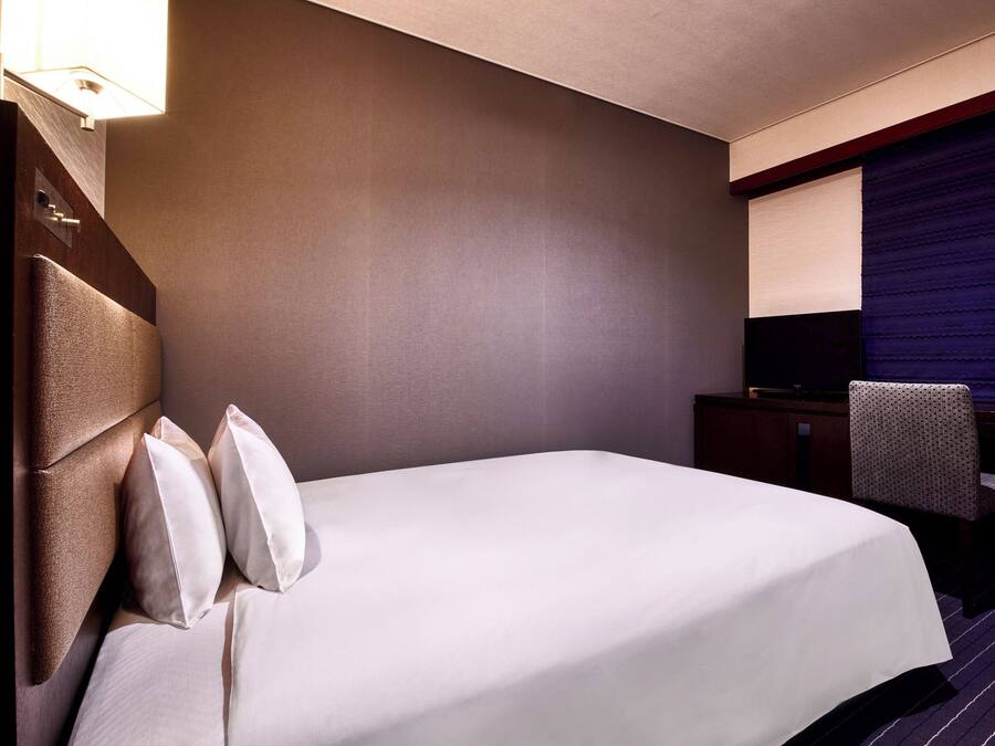 A hotel room with a large bed, a flat-screen TV, a desk, and a chair.