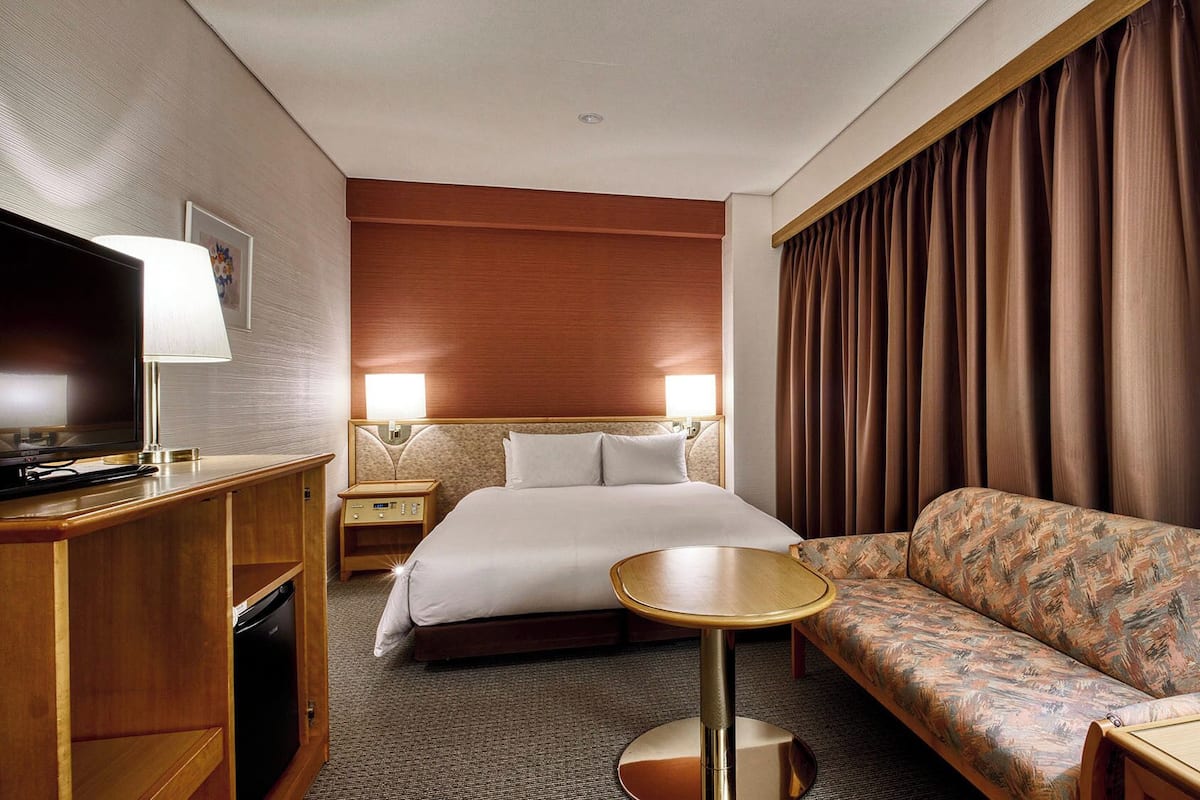 Une chambre d’hôtel avec un lit, un canapé, une tél évision, une lampe et une petite table.