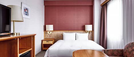 A hotel room with a bed, a TV, a desk, a chair, and a sofa.