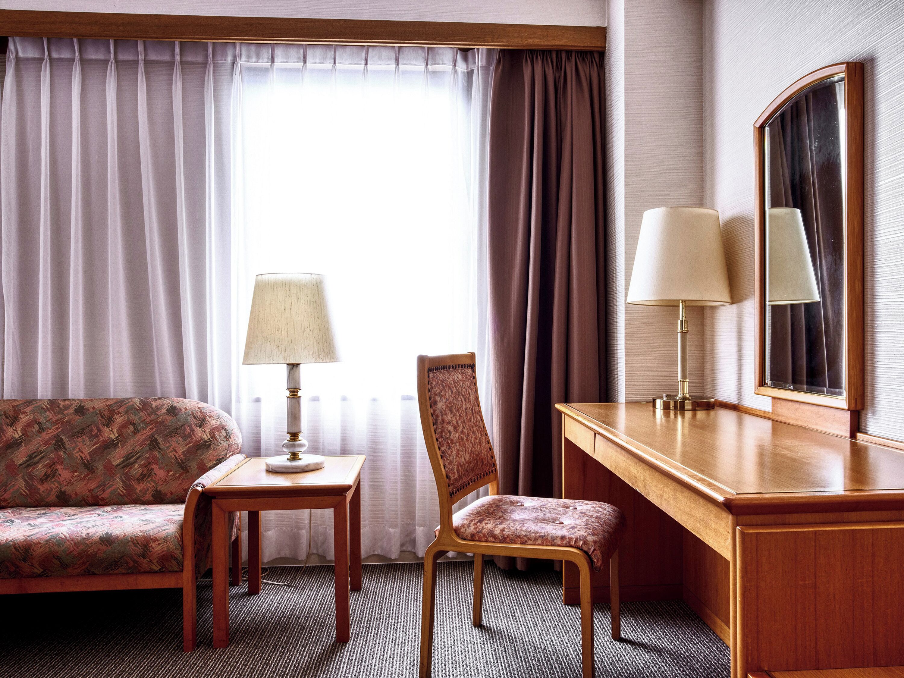 A hotel room with a sofa, a chair, a desk, and two lamps.