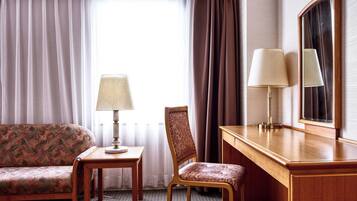 A hotel room with a sofa, a chair, a desk, and two lamps.