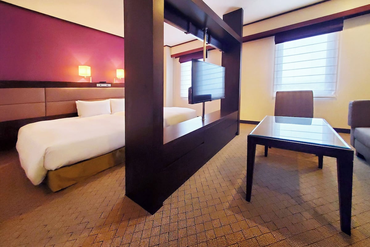 Une chambre d’hôtel équipée d’un lit, d’un bureau, d’une chaise, d’une télévision et d’une fenêtre avec des stores.