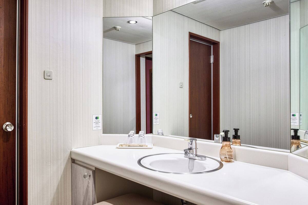 Une salle de bain avec une porte en bois, un lavabo blanc, un miroir et un porte-serviettes.