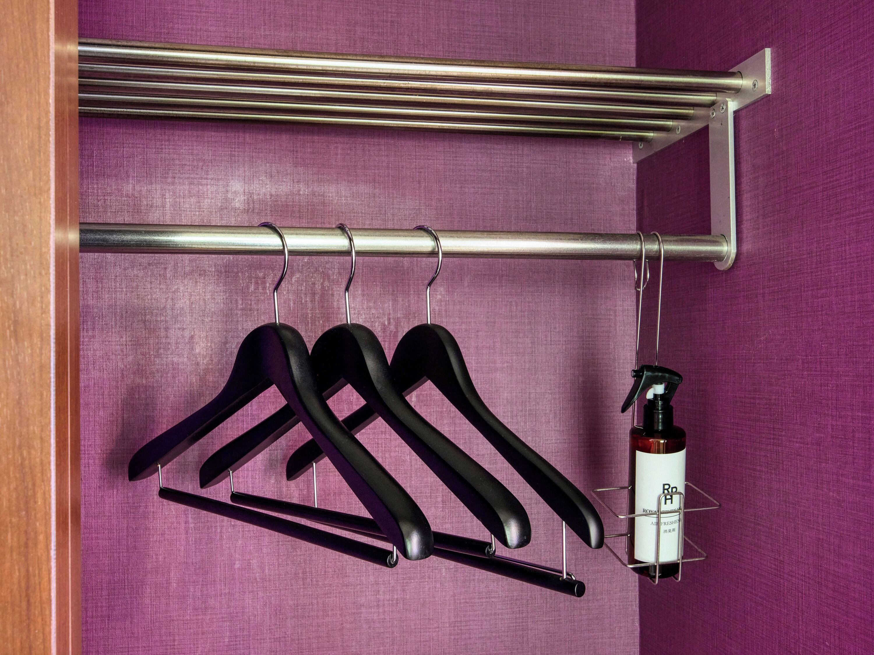 A metal rod with three black hangers and a bottle of hand sanitizer attached to it.