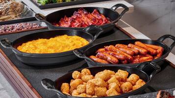 A buffet with various dishes including scrambled eggs, bacon, sausages, and tater tots.