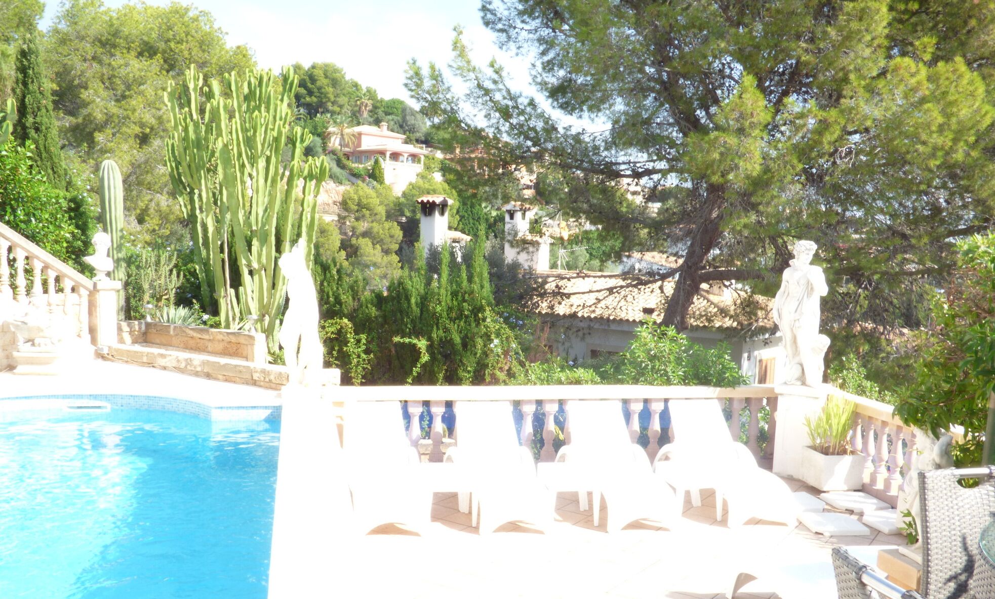 A pool area with a stone balustrade, a statue, and cacti.