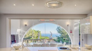 A modern interior with a large arched glass door leading to an outdoor patio with a view of the sea. - Villa Ocean View en Portals Nous by Mallorca North Villas (Portals Nous)