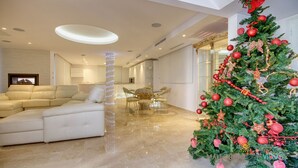 A modern living room with a beige sofa, a dining area with a glass table and chairs, and a Christmas tree with red ornaments. - Villa Ocean View en Portals Nous by Mallorca North Villas (Portals Nous)