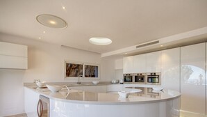 A modern kitchen with a central island, built-in ovens, and a large window. - Villa Ocean View en Portals Nous by Mallorca North Villas (Portals Nous)