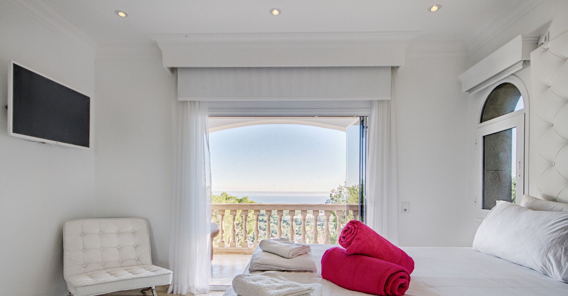 A bedroom with a bed, a chair, a TV, and a balcony with a view.
