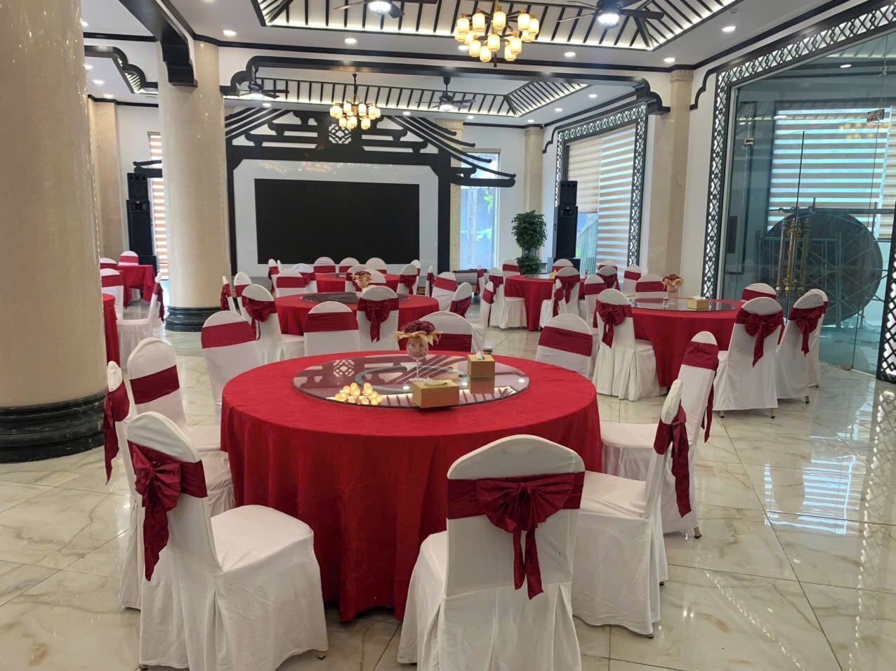 A banquet hall with round tables, white chairs with red sashes, and a central stage.