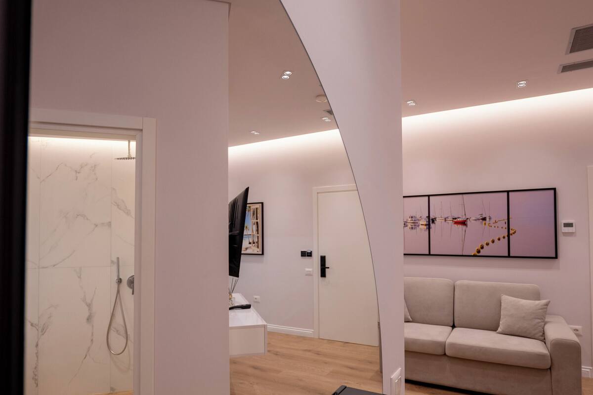 A modern interior with a wooden floor, a black bench, a beige sofa, and a wall-mounted TV.