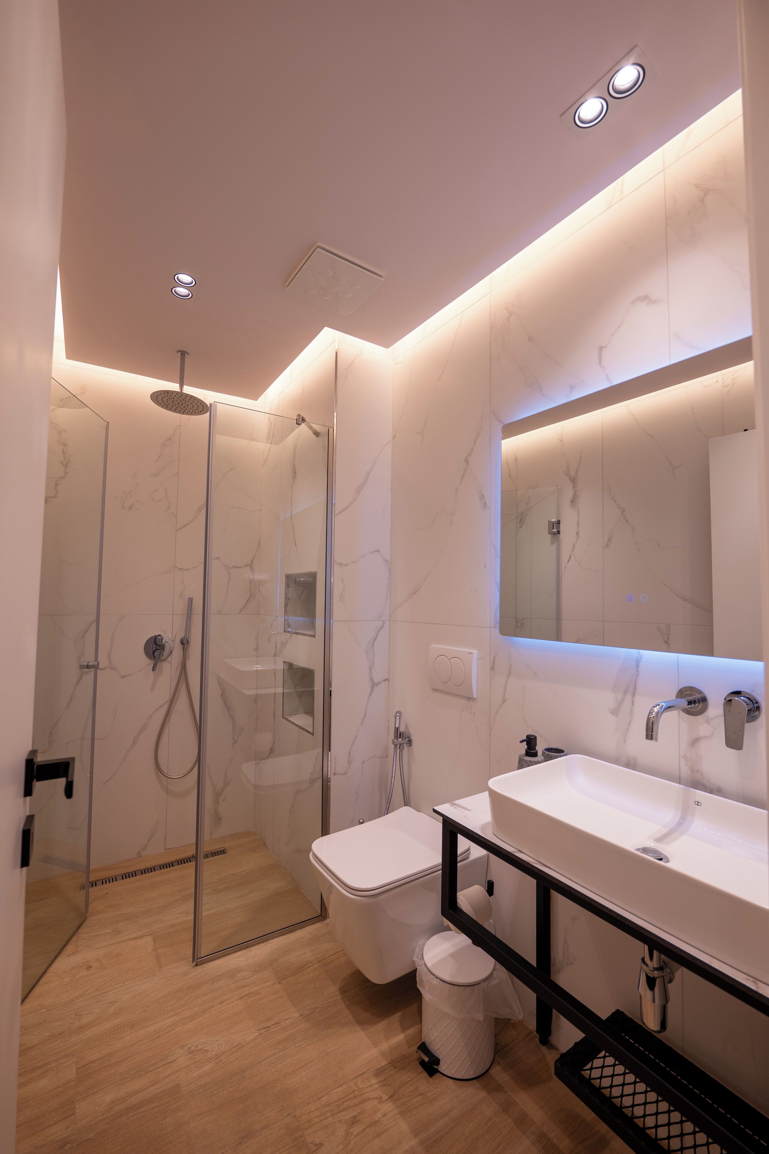 A modern bathroom with a glass-enclosed shower, a white sink, and a large mirror.