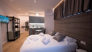 Et moderne hotelværelse med en stor seng, et fjernsyn, et skrivebord og et badeværelse i baggrunden.