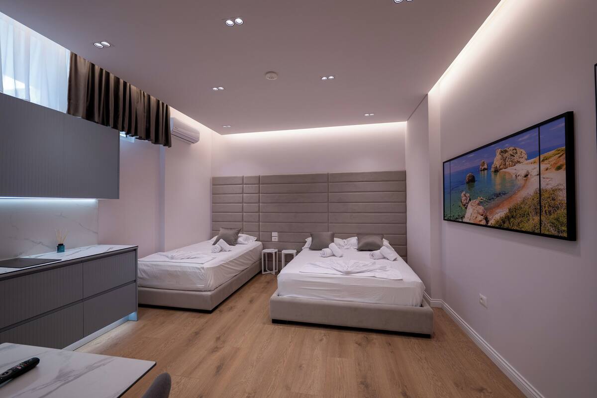 A modern bedroom with two beds, a desk, and a large window.