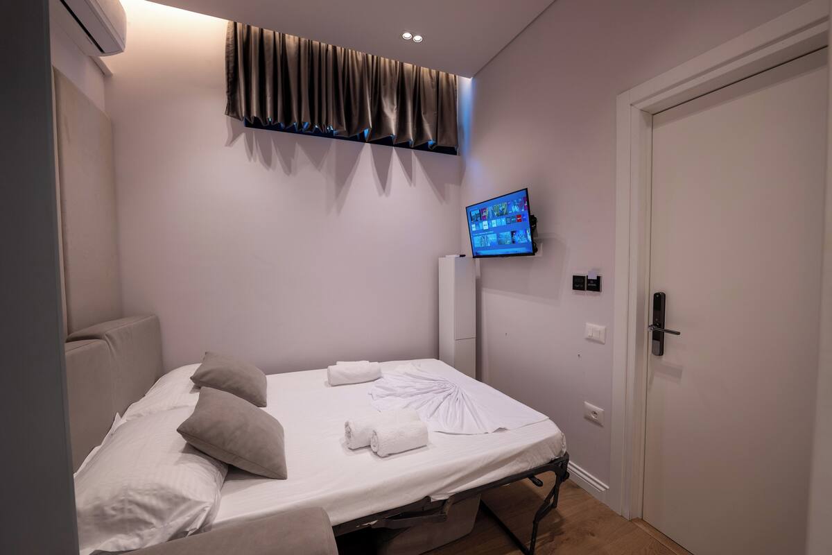 A bedroom with a bed, pillows, a TV, an air conditioner, and a door.