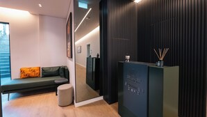 Et moderne receptionsområde med en sort skranke, en grøn sofa med pude i orange, og et trægulv.