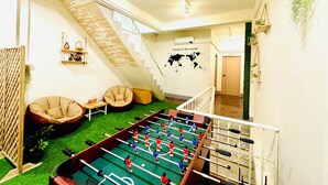 Une pièce avec une table de baby-foot, deux fauteuils en forme de poire, un escalier et une carte géographique murale.