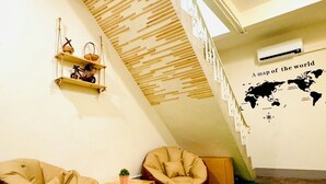 Une pièce avec une moquette verte, une carte du monde accrochée au mur, une étagère en bois ornée d’objets décoratifs et un escalier.