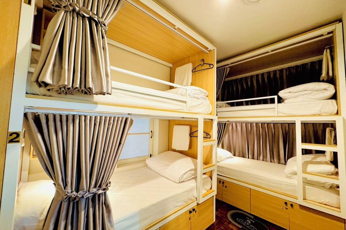 A bunk room with three beds, each with a curtain, and a wardrobe with hanging clothes.