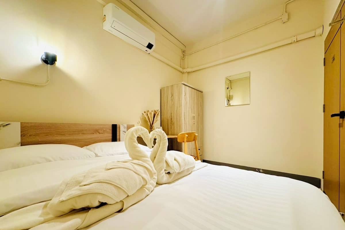 A hotel room with a bed, a wooden headboard, a wardrobe, a mirror, and an air conditioning unit.