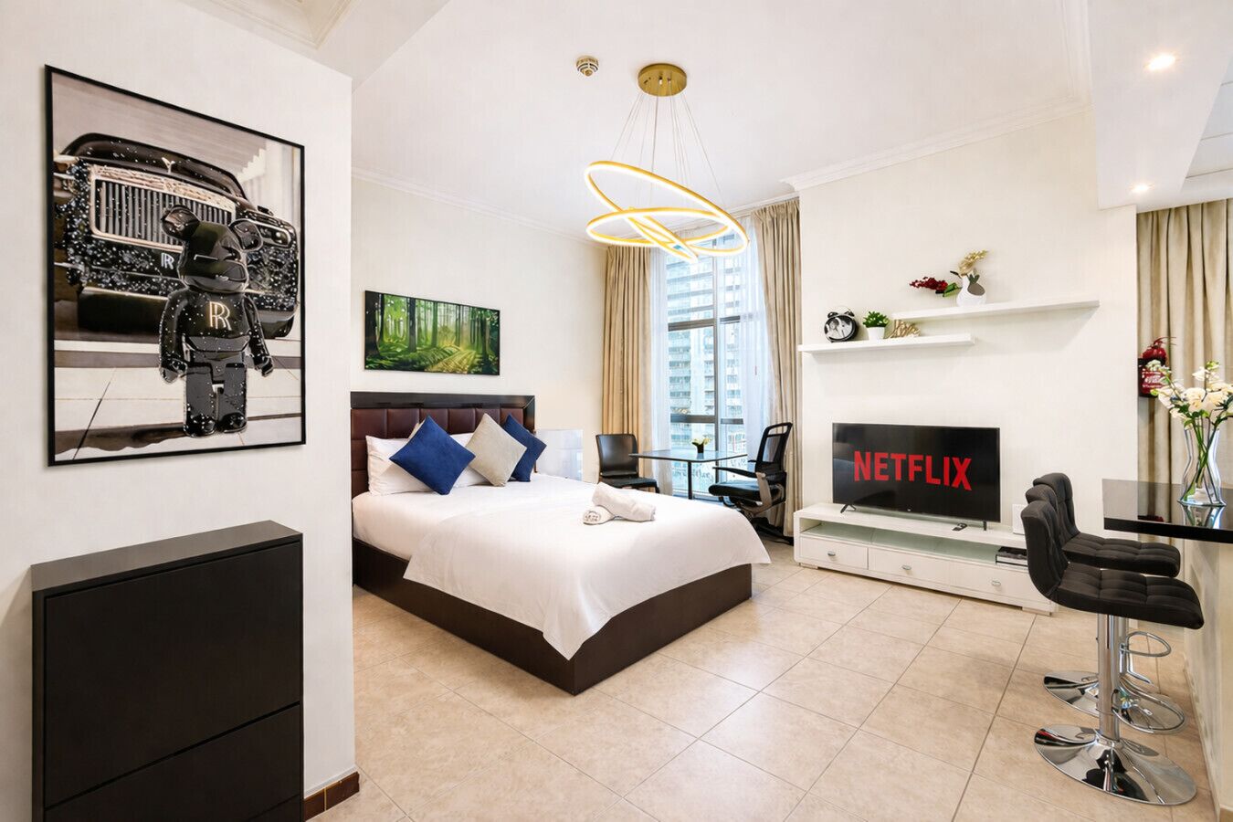 A modern hotel room with a bed, a desk with a computer, a TV, and a large window.
