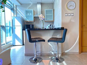 A modern kitchen with two bar stools, a clock, and a vase with flowers.