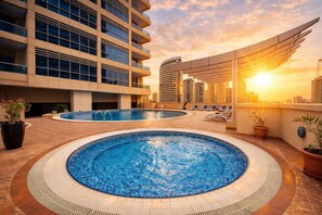 Un espace piscine sur le toit, comprenant deux piscines, des chaises longues et un bâtiment moderne doté de balcons.