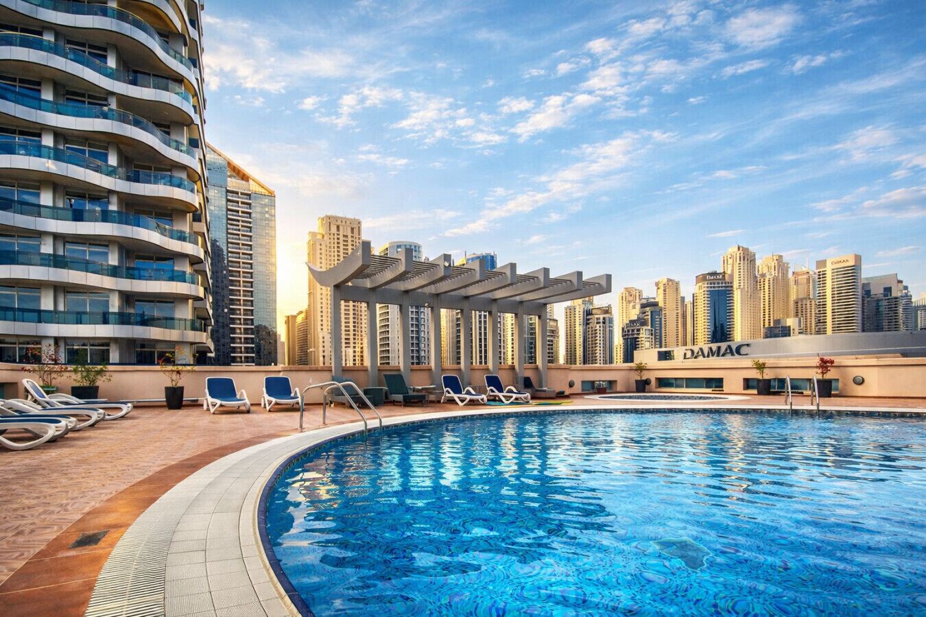 A swimming pool with lounge chairs, a pergola, and a city skyline in the background.